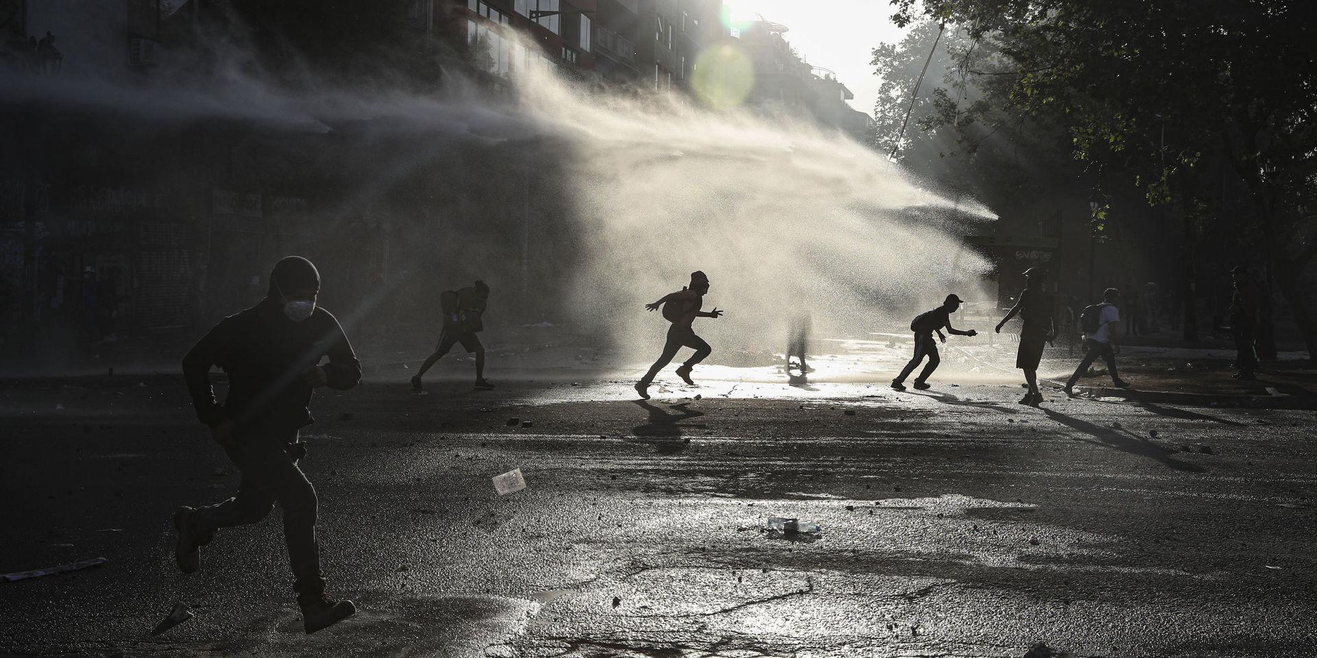 Demonstranter springer genom polisens vattenkanoner under demonstrationer mot Chiles regering i huvudstaden Santiago.