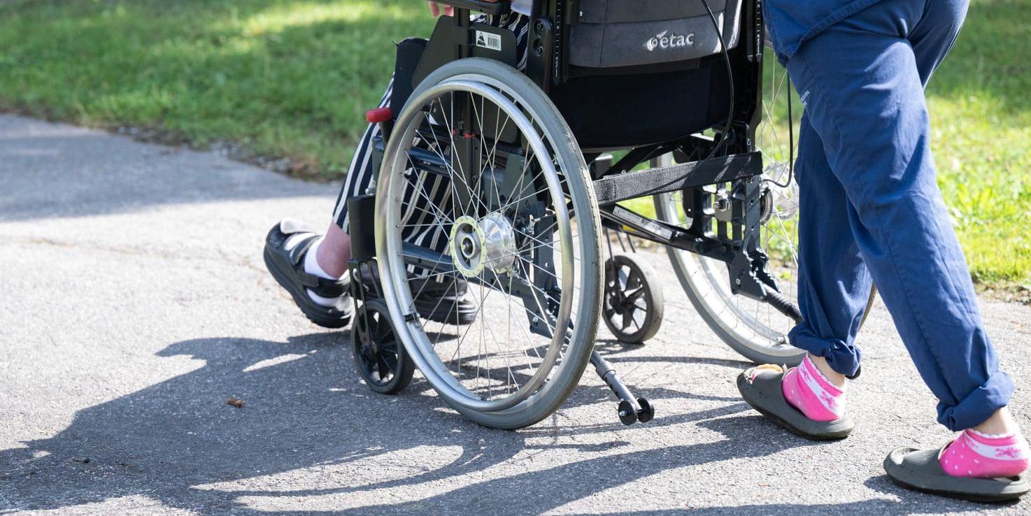 En person i rullstol puttas framåt av en vårdare.