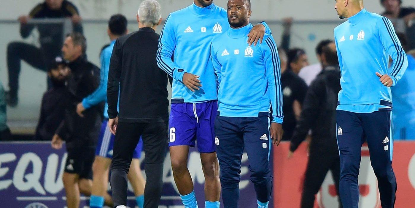 Patrice Evra (mitten) leds bort av lagkamraten Rolando (vänster) efter att ha bråkat med Marseilles fans.