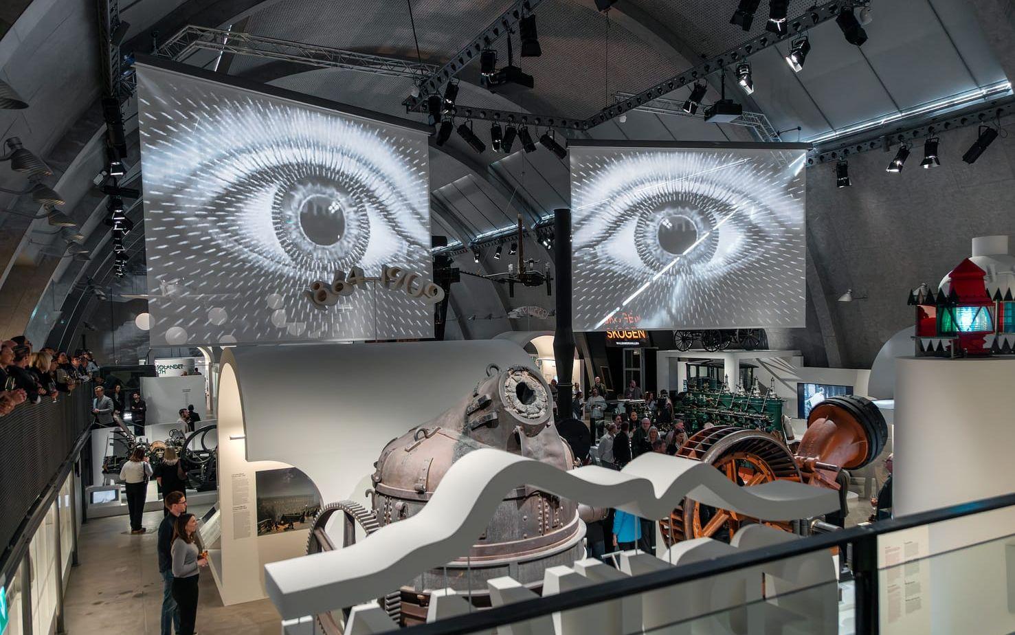 På två skärmar i taket visas med jämna mellanrum det nya audiovisuella verket ”Teknika & neutika” av Try New Things med fokus på människorna och på hur deras liv påverkas av den snabba tekniska utvecklingen. Pressbild. 