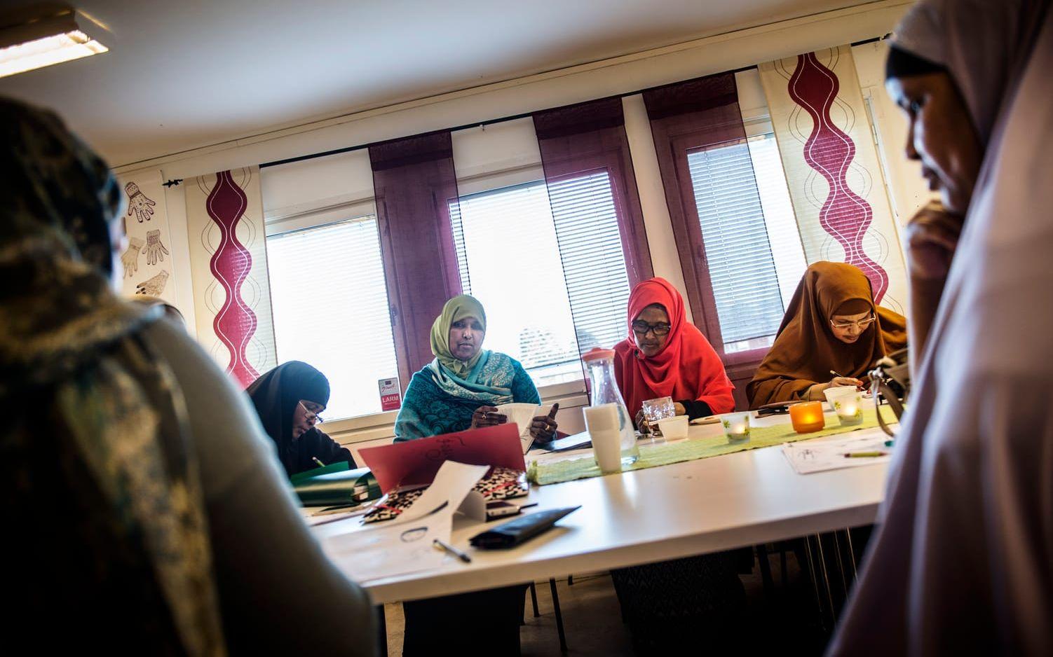 Asha Ali Husein i rött koncentrerar sig under lektionen i svenska på Kvinnorcenter Bergsjön. Bild: Jenny Ingemarsson.