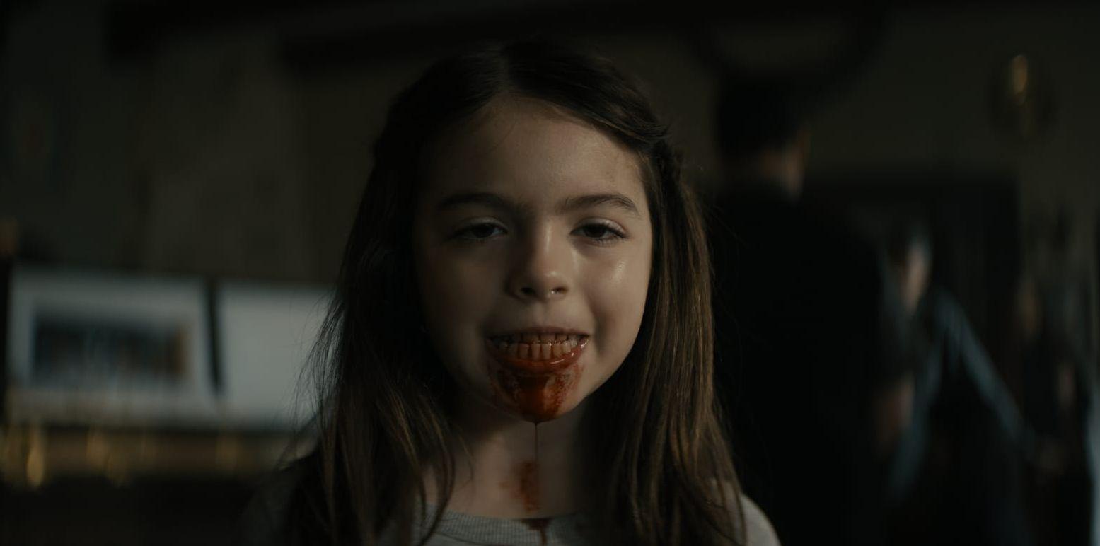 En liten flicka ler ett elakt leende medan blod rinner ur munnen på henne.