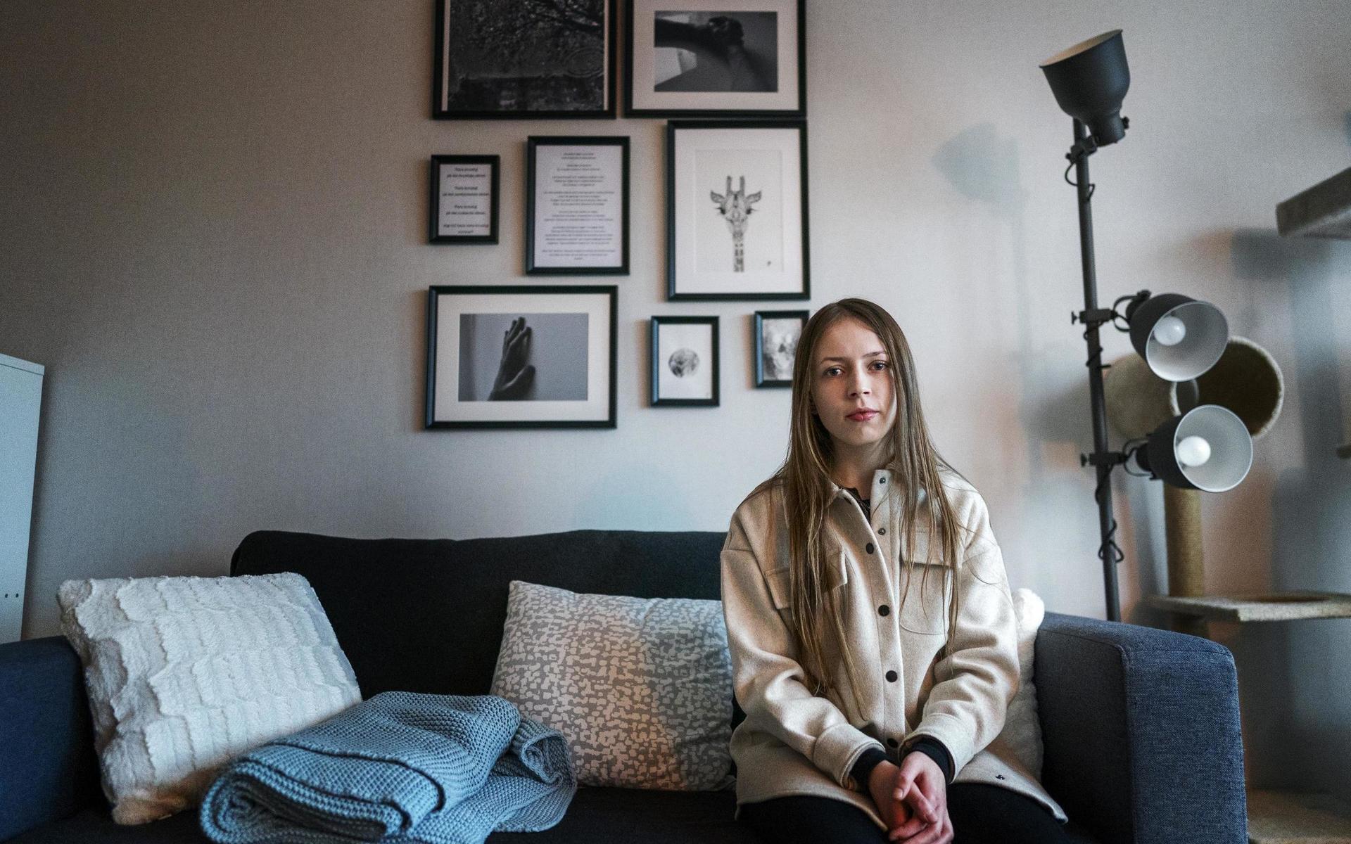 Carmen Jedrzejak sitter i sin soffa. Hon arbetar sällan hemifrån med sin konst, men bakom henne på väggen hänger delar av utställningen ”#Uppskattadhorunge” som visades på Blå stället i höstas.